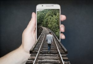 Ve fotokoláži vchází muž po kolejích do mobilního telefonu, kde koleje pokračují zelení do dálky.
